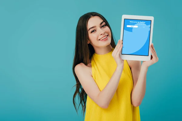 KYIV, UKRAINE - 6 JUIN 2019 : heureuse belle fille en robe jaune montrant tablette numérique avec application twitter isolée sur turquoise — Photo de stock