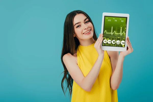 Hermosa chica feliz en vestido amarillo mostrando tableta digital con aplicación sanitaria aislada en turquesa - foto de stock