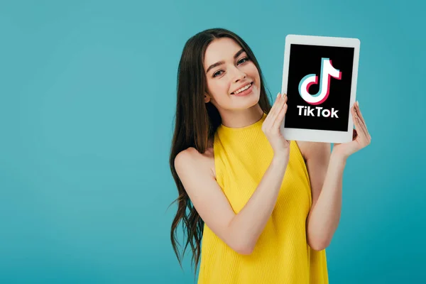 KYIV, UCRAINA - 6 GIUGNO 2019: felice bella ragazza in abito giallo che mostra tablet digitale con app tik tok isolata su turchese — Foto stock