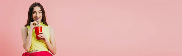 Красивая улыбающаяся девушка в яркой одежде пьет содовую из соломы, изолированной на розовый, панорамный горячий — стоковое фото