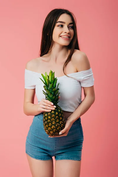 Vista cortada de bela menina sorridente segurando abacaxi delicioso maduro isolado em rosa — Fotografia de Stock