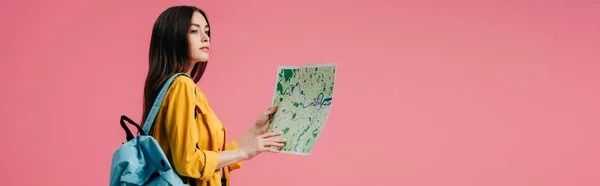 Panoramic shot of dreamy girl with backpack holding map and looking away isolated on pink — Stock Photo