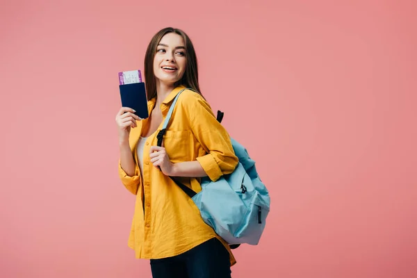 Hermosa chica sonriente con mochila con pasaporte con billete de avión aislado en rosa - foto de stock