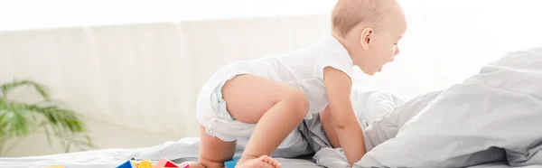 Panoramic shot of happy little child in diaper crawling on white bed — Stock Photo