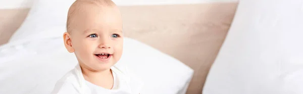 Foto panorámica de un lindo niño pequeño con ojos azules sonriendo en una habitación blanca - foto de stock