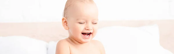 Panoramic shot of cute little child laughing with closed eyes in white room — Stock Photo