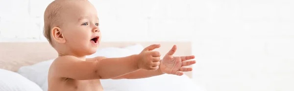 Panoramic shot of adorable little child opening mouth and raising hands forward in white room — Stock Photo