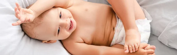 Colpo panoramico di bambino scalzo in pannolino sdraiato sul letto con biancheria da letto bianca e sorridente — Foto stock