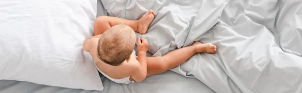 Panoramic shot of little barefoot child sitting on bed with white bedding — Stock Photo