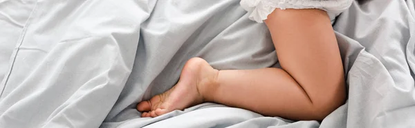 Panoramic shot of cute barefoot baby leg on white sheets — Stock Photo