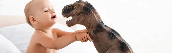 Panoramic shot of cute little child playing with brown dinosaur in white room — Stock Photo