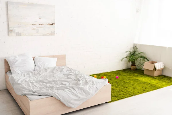 Habitación luminosa con cama doble y caja de cartón cerca de la planta en alfombra verde - foto de stock