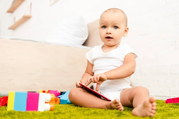 Adorable child sitting on green floor and pointing with finger on digital device — Stock Photo