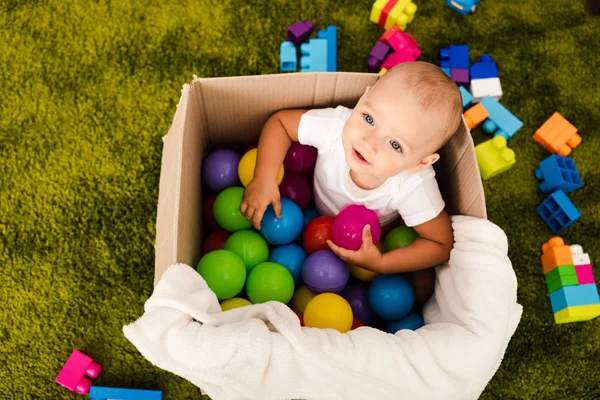 Vista superior de niño lindo en caja de cartón jugando con bolas de colores - foto de stock
