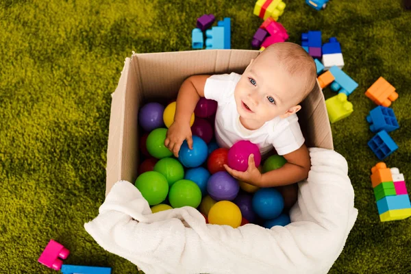 Blick von oben auf niedliches Kind im Karton, das mit bunten Kugeln spielt — Stockfoto