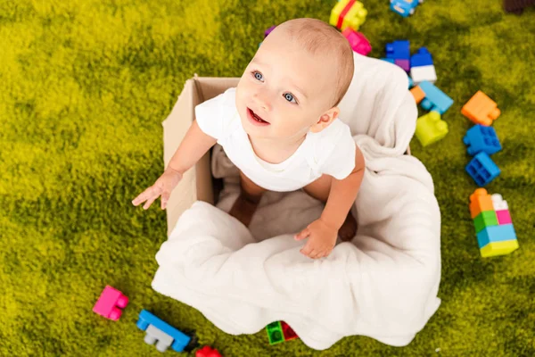 Вид сверху симпатичного маленького ребенка в картонной коробке с белым одеялом — стоковое фото