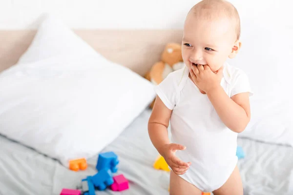 Cute little child standing on white bed, looking away and smiling — Stock Photo