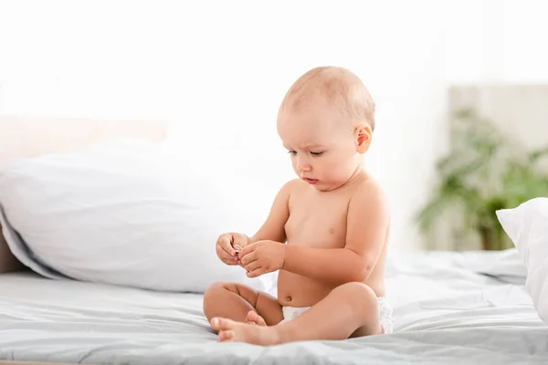 Cute barefoot child in diaper sitting on bed in ligth room — Stock Photo