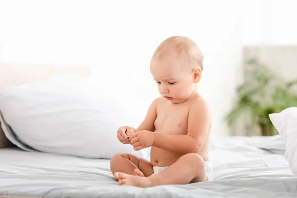 Carino a piedi nudi bambino in pannolino seduto sul letto in camera ligth — Foto stock