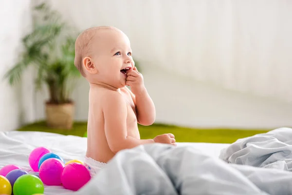 Criança bonita sentada na cama, sorrindo e tomando o dedo na boca — Fotografia de Stock