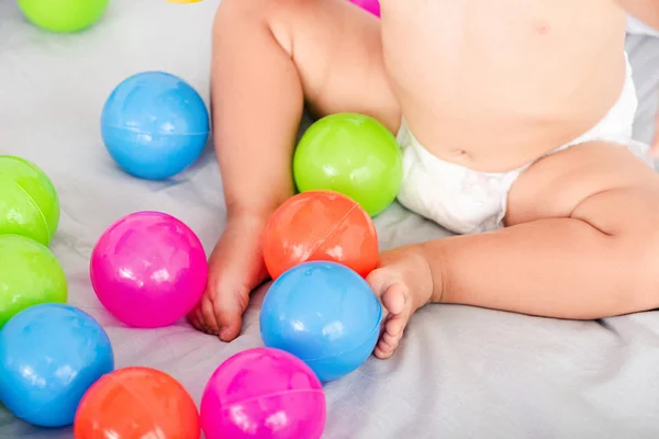 Vista recortada de lindas piernas de bebé en la cama entre bolas de colores - foto de stock