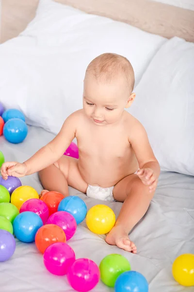 Top view of cute little baby sitting on bed among colored balls — Stock Photo