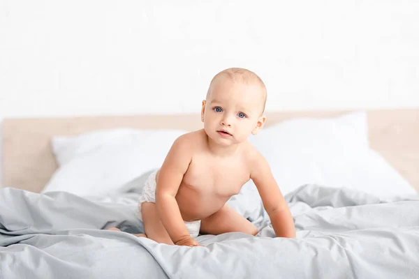 Mignon petit enfant assis sur un lit blanc et regardant la caméra — Photo de stock