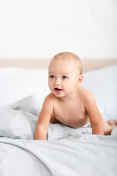 Criança pequena bonito rastejando em roupas de cama brancas e olhando para longe — Fotografia de Stock