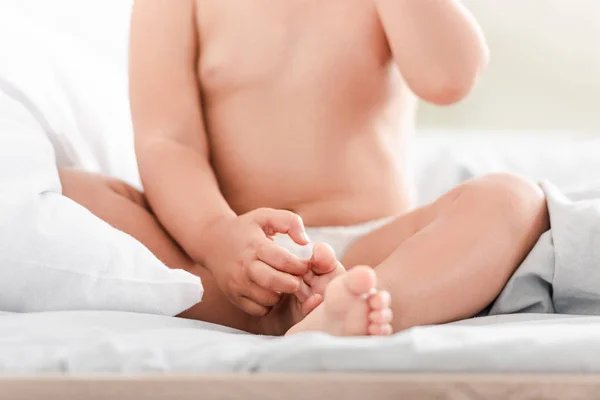 Vista cortada de criança pequena com dedos minúsculos dos pés e dedos sentados na cama branca — Fotografia de Stock