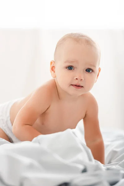 Criança pequena bonito rastejando em tecido branco e olhando para a câmera — Fotografia de Stock