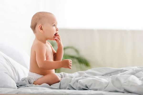 Vue latérale du bébé regardant loin et prenant les doigts dans la bouche — Photo de stock