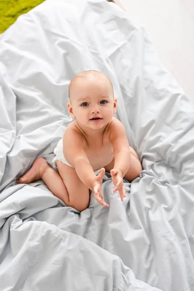 Lindo bebé en pañal sentado en la cama y mirando a la cámara - foto de stock