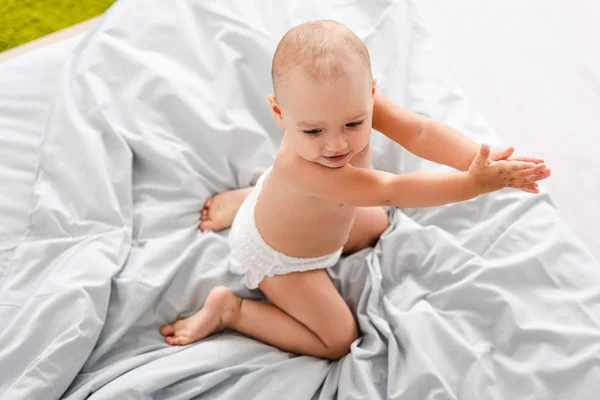 Visão superior do bebê na fralda sentado na cama e palmas das mãos — Fotografia de Stock