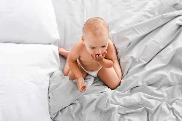 Top view of baby sitting on white sheets and covering mouth with hand — Stock Photo
