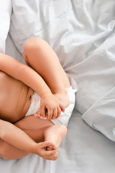 Vista cortada de bebê em fralda deitada nas costas e agarrando os pés com as mãos — Fotografia de Stock