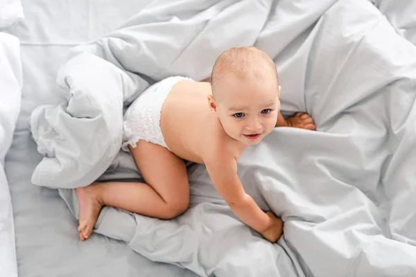 Top view of adorable little baby crawling on white sheets — Stock Photo