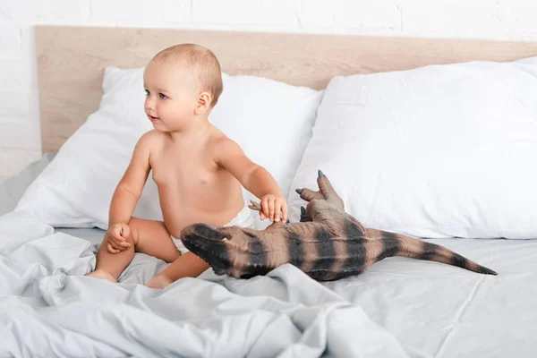 Cute little child sitting on bed and holding brown toy dinosaur — Stock Photo