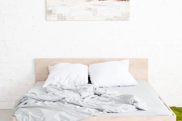 Wooden bed with two white pillows and crumpled blanket in light room — Stock Photo