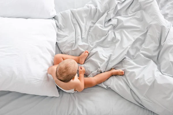 Вид зверху маленька дитина сидить на ліжку зі збитою світлою ковдрою — стокове фото