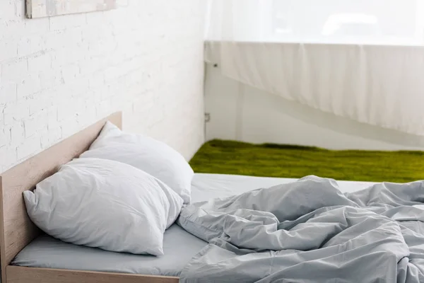 Cama de madeira com travesseiros e cobertor de luz amassada na sala branca com tapete verde — Fotografia de Stock