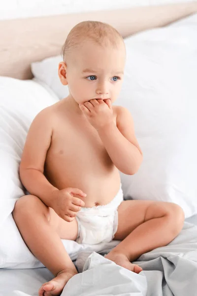 Adorable little child sitting on bed with soft white pillows — Stock Photo