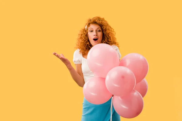 Überrascht rothaarige Mädchen mit rosa Luftballons isoliert auf gelb — Stockfoto