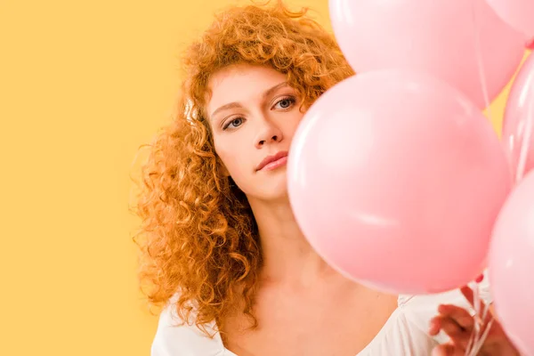 Schöne junge rothaarige Frau mit rosa Luftballons isoliert auf gelb — Stockfoto