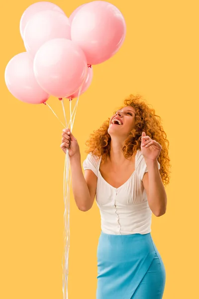 Femme rousse gaie avec des ballons roses isolés sur jaune — Photo de stock