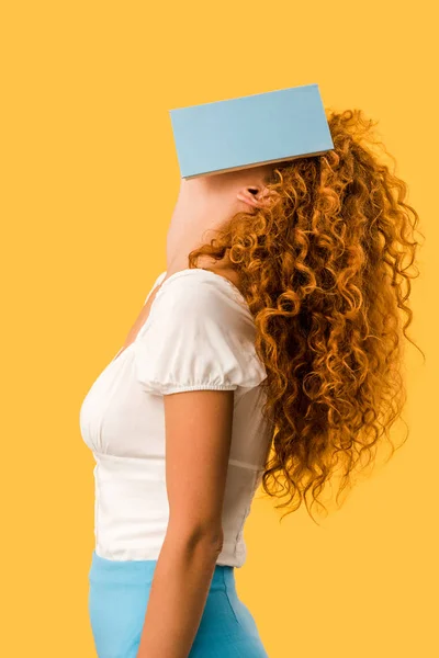 Mujer pelirroja estudiante con libro en la cara aislado en amarillo - foto de stock