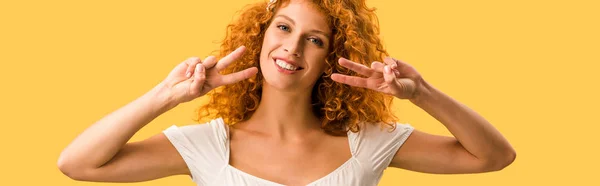 Mujer sonriente con el pelo rojo mostrando símbolos de paz aislados en amarillo - foto de stock