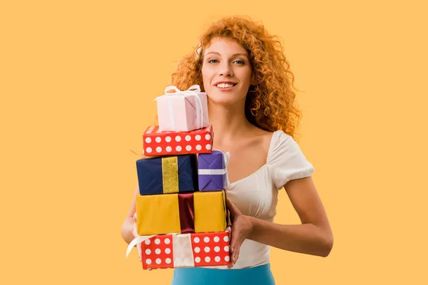 Attractive redhead girl holding gift boxes isolated on yellow — Stock Photo