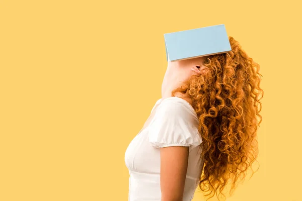 Estudante ruiva com livro no rosto isolado no amarelo — Fotografia de Stock