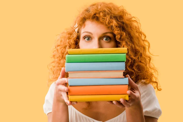 Mujer pelirroja estudiante sosteniendo libros aislados en amarillo - foto de stock