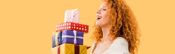 Laughing redhead girl holding presents isolated on yellow — Stock Photo